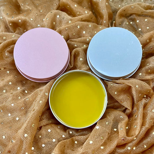 Three tins with lids on a textured brown fabric background